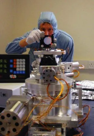 Technician in clean-room clothing aligning an instrument with a micro-alignment telescope